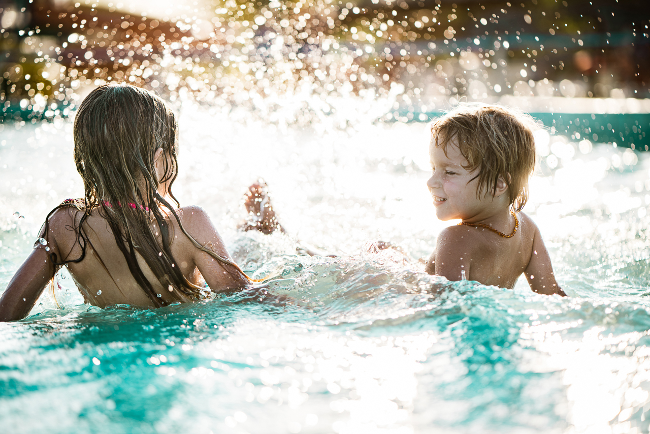Back view small girl and boy sitting and splashing in swimming pool