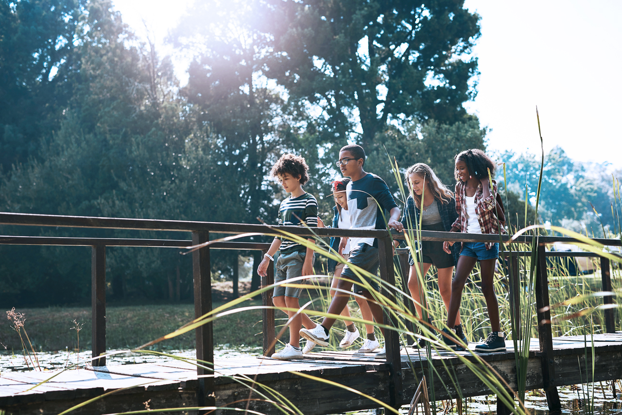 Shot of a group of teenagers walking across a bridge in nature at summer camp